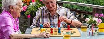 Zwei ältere Damen sitzen draußen an einem Tisch und spielen ein Brettspiel